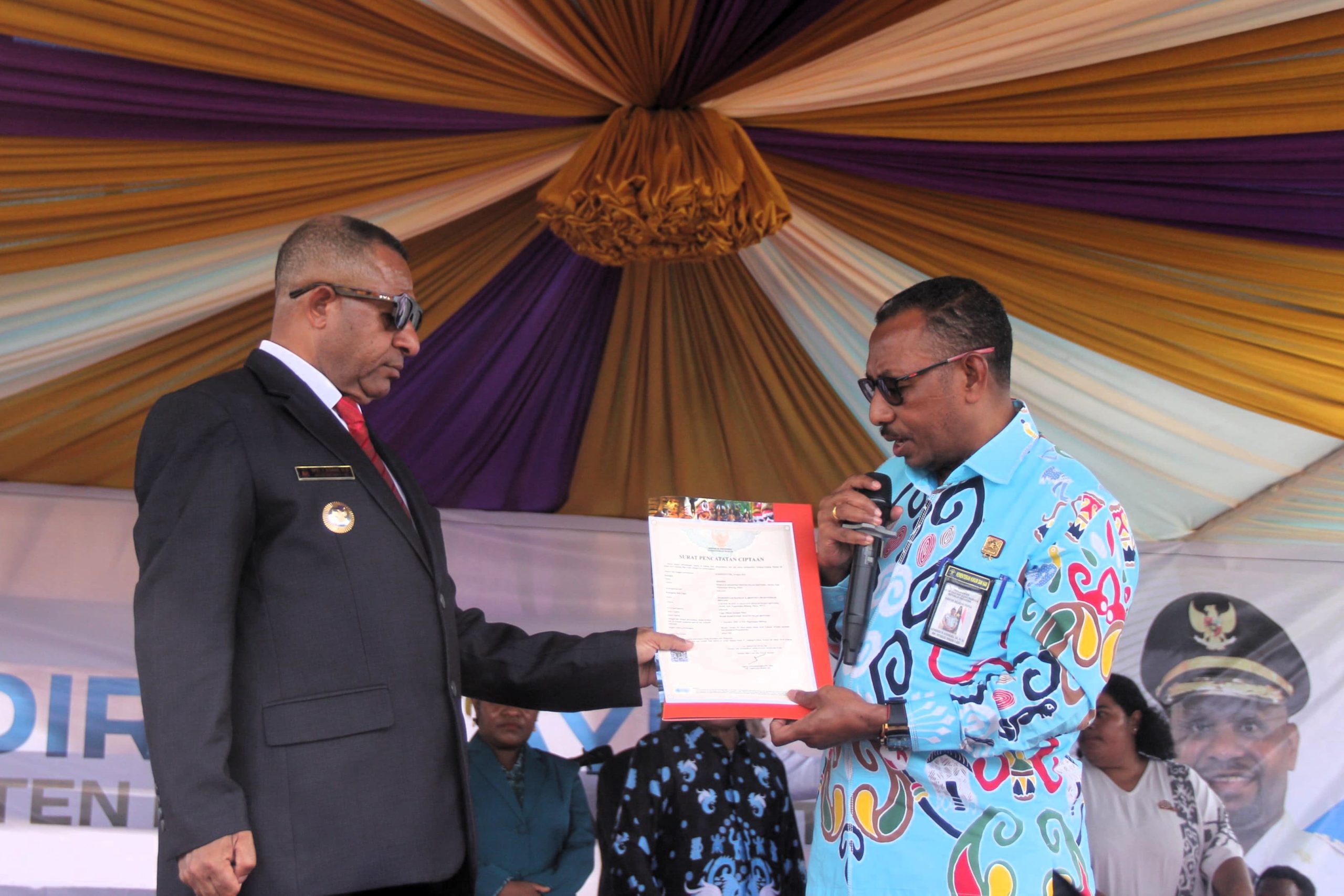 Kakanwil Kemenkum Provinsi Papua, Anthonius Mathius Ayorbaba, SH,M.Si menyerahkan Sertifikat Hak Cipta dari lagu Mars Pegunungan Bintang kepada Bupati Spei Yan Bidana, ST,M.Si di sela-sela perayaan HUT Kabupaten Pegunungan Bintang ke-22 di Halaman Kantor Bupati, Sabtu (22/04/2025).